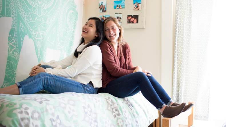 Two students sitting on a bed in a dorm