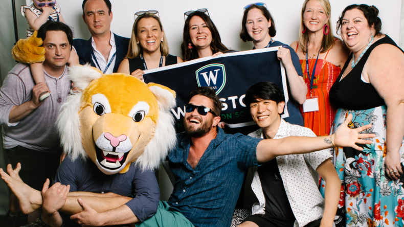 A group of people posing with the school banner and mascot